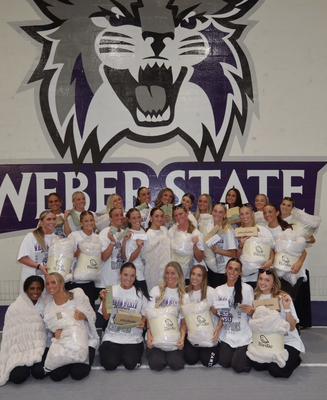 Weber State dance team celebrating with Birdie blankets in front of the Wildcats mural